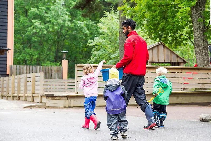 En förskollärare och några förskolebarn på en förskolegård